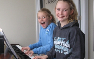 Two students playing on piano with big smiles